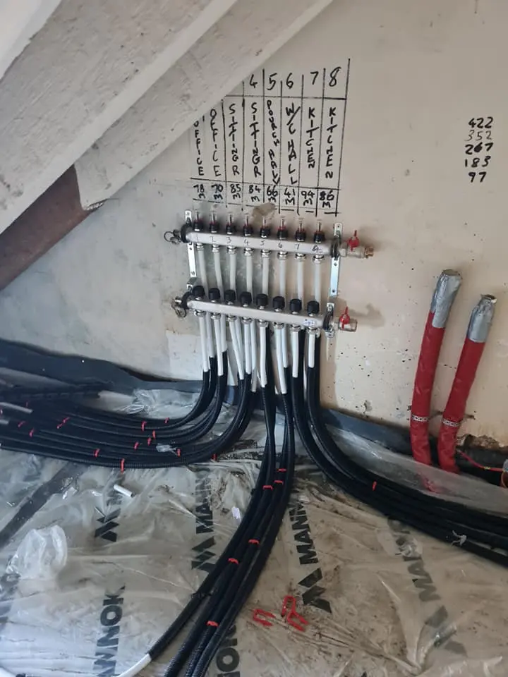 Underfloor heating manifold with handwritten room labels showing zone control setup